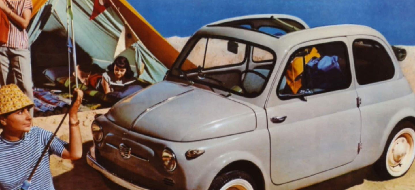 Se muestra un dibujo vintage de un Fiat Cabrio gris clásico en una playa con gente que acampa cerca.