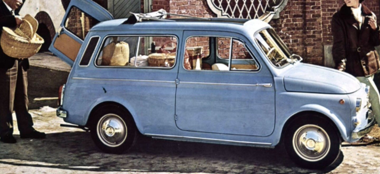 Se muestra un dibujo "vintage" de un clásico Fiat Wagon celeste con el portón trasero de apertura lateral abierto, un hombre de pie junto a la puerta abierta sosteniendo una cesta de picnic y una mujer parada en la parte delantera.