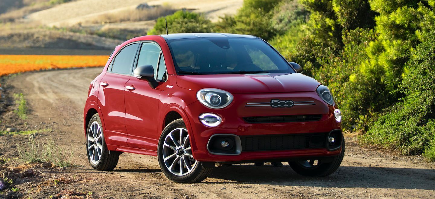 Display A three-quarter front view of a red 2022 Fiat 500X Sport parked on a dirt road with vineyards in the background.