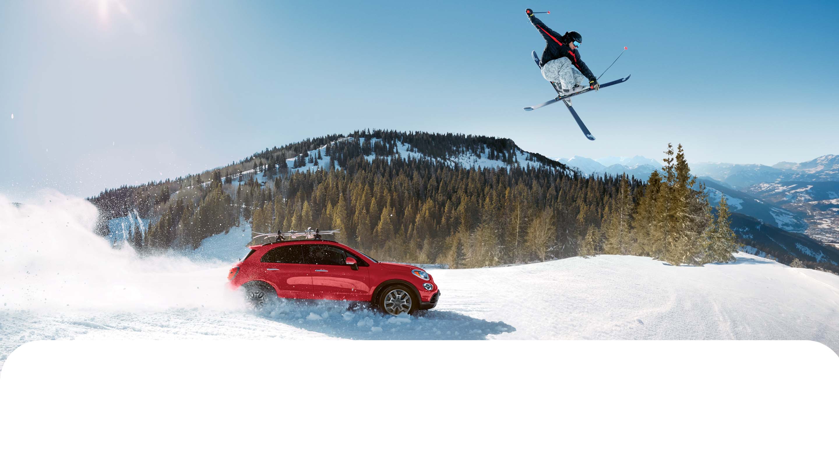 Perfil del lado del pasajero de un Fiat 500X Trekking 2022 rojo con equipamiento no original, circulando por un camino cubierto con mucha nieve, levantando polvo blanco mientras avanza, con un esquiador saltando por encima del vehículo e imponentes montañas de fondo.